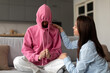 Stubborn teenage girl putting hood on head avoiding mom apology, ignoring talk with parent sitting on couch at home. Teen girl introvert hiding in hoodie