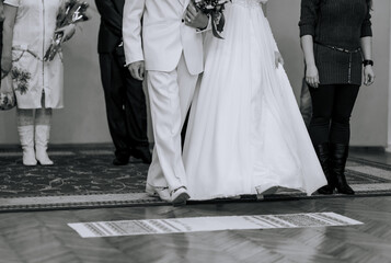 Wall Mural - The bride and groom walk, stepping on an embroidered towel at the ceremony. Wedding photography, Ukrainian tradition, ritual. Black and white.