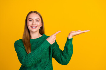 Photo of young happy lady wearing green pullover hold copy space arm demonstrating new mobile app isolated on yellow color background