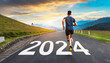 New year 2024 concept, beginning of success. Text 2024 written on asphalt road and male runner preparing for the new year. Concept of challenge or career path and change