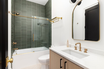 Wall Mural - A bathroom with a wood vanity cabinet, gold hardware and faucet, and a shower with green subway tiles. No brands or labels.