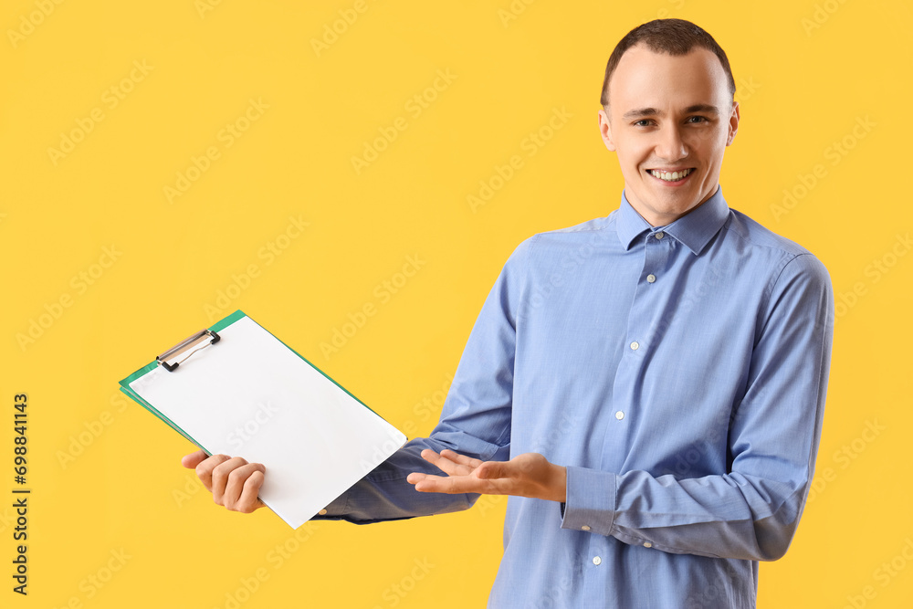 Young man with clipboard on yellow background