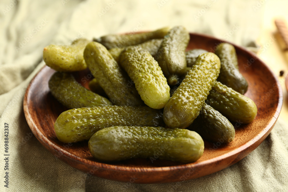 Wooden plate with tasty pickled cucumbers on yellow background