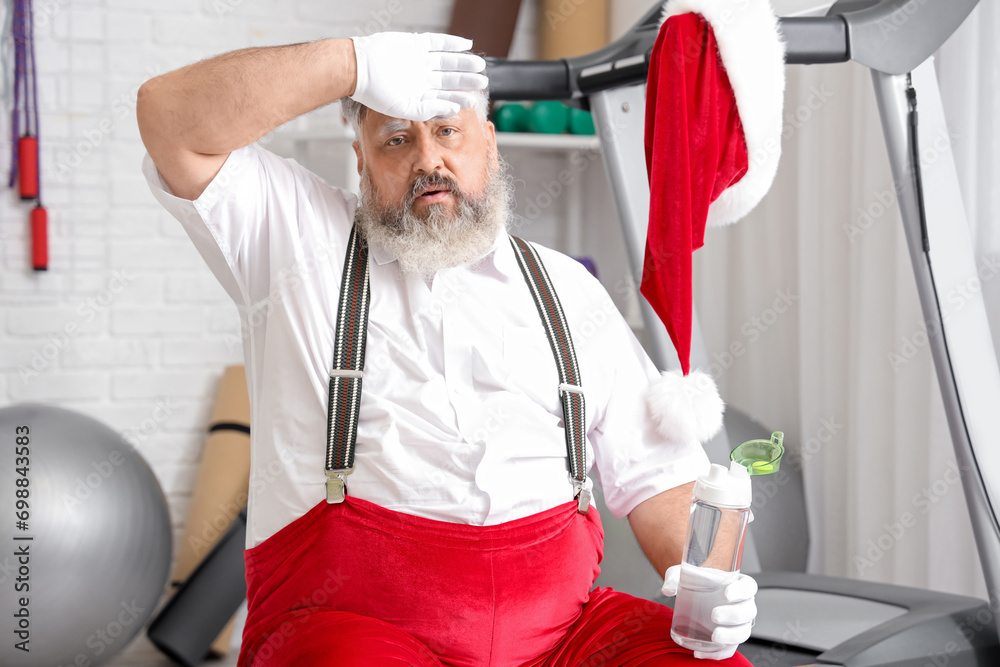 Tired Santa Claus with water bottle after training in gym