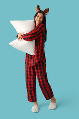 Sticker - Beautiful young woman in checkered pajamas and reindeer horns with soft pillow on blue background