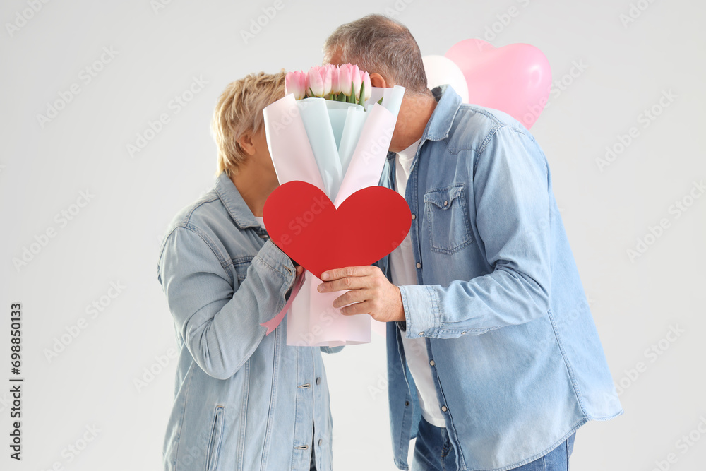 Mature couple with paper heart and tulips on light background. Valentine's Day celebration