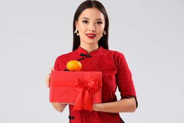 Poster - Young Asian woman with mandarin and gift box on light background. Chinese New Year celebration