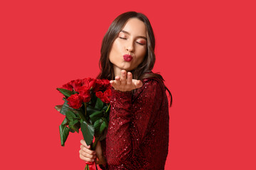 Poster - Beautiful young woman blowing kiss with bouquet of roses on red background. Valentine's Day celebration