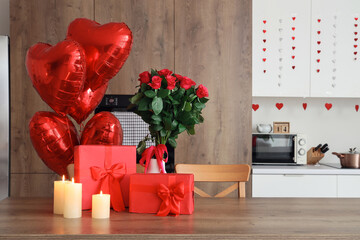 Poster - Burning candles, gift boxes and bouquet of roses on wooden table in kitchen, closeup. Valentine's Day celebration