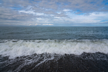 An incoming wave on the Black Sea and a pebble beach on the Sochi coast on a summer day with clouds, Sochi, Krasnodar Territory, Russia