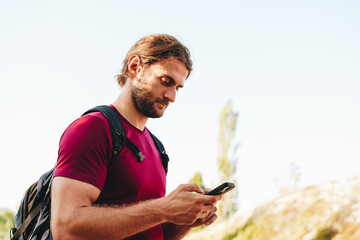 Hiker man with backpack checks the route on his phone on the walking trail