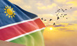 Waving flag of Namibia against the background of a sunset or sunrise. Namibia flag for Independence Day. The symbol of the state on wavy fabric.