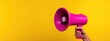 Hand holding bright pink megaphone on yellow background for advertising campaign