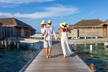 a beautiful family walks over a wooden pier between water lodges in the maldives islands during thei
