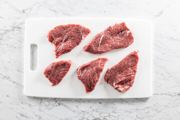 Wall Mural - Raw fresh beef  meat cut into steaks on a white cutting board - Top of view.