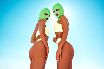 Two beautiful sexy women in green underwear. Models wearing bandit balaclava mask. Hot seductive female in nice lingerie posing in the street at sunny day, blue sky. Crime and violence. Perfect body