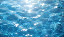 Blue Water Surface With Ripples And Sun Reflections. Abstract Background.