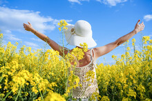 Woman On Her Back With Her Arms Raised In A Field Of Yellow Flowers. Concept Of Freedom In Spring