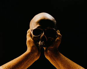 Wall Mural - Hands with human skull on black. Golden sands, time concept. Symbolism, mortality