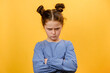 Portrait of grumpy preteen girl child pouting lips, grimacing and looking angrily at camera, posing isolated over plain yellow color background wall in studio. People emotion lifestyle concept