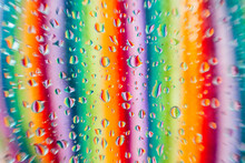 Water Droplets On A Glass Surface With A Blurred Background Showcasing A Spectrum Of Colors In Vertical Lines