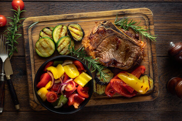 Wall Mural - Juicy cooked grilled beef steak with vegetables on a wooden cutting board on a dark stone background, top view