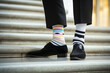 Legs with black pants, different pair of socks and black shoes standing on stairs outdoors. Young man foots in mismatched socks. Odd Socks day, Anti-Bullying Week, Down syndrome awareness concept