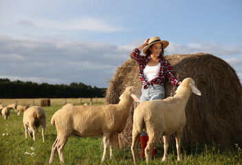 Wall Mural - Smiling woman and sheep near hay bale on animal farm. Space for text