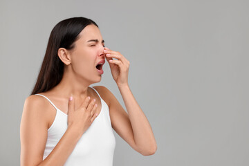 Canvas Print - Suffering from allergy. Young woman sneezing on light grey background, space for text