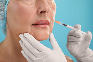 Sticker - Doctor giving facial injection to senior woman on light blue background, closeup. Cosmetic surgery