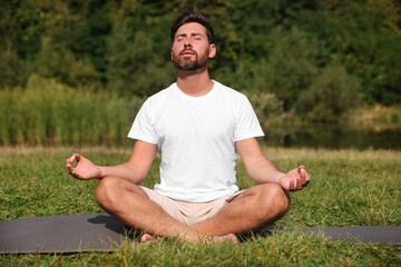 Sticker - Man practicing yoga on mat outdoors. Lotus pose