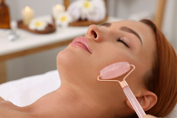 Poster - Young woman receiving facial massage with rose quartz roller in beauty salon, closeup