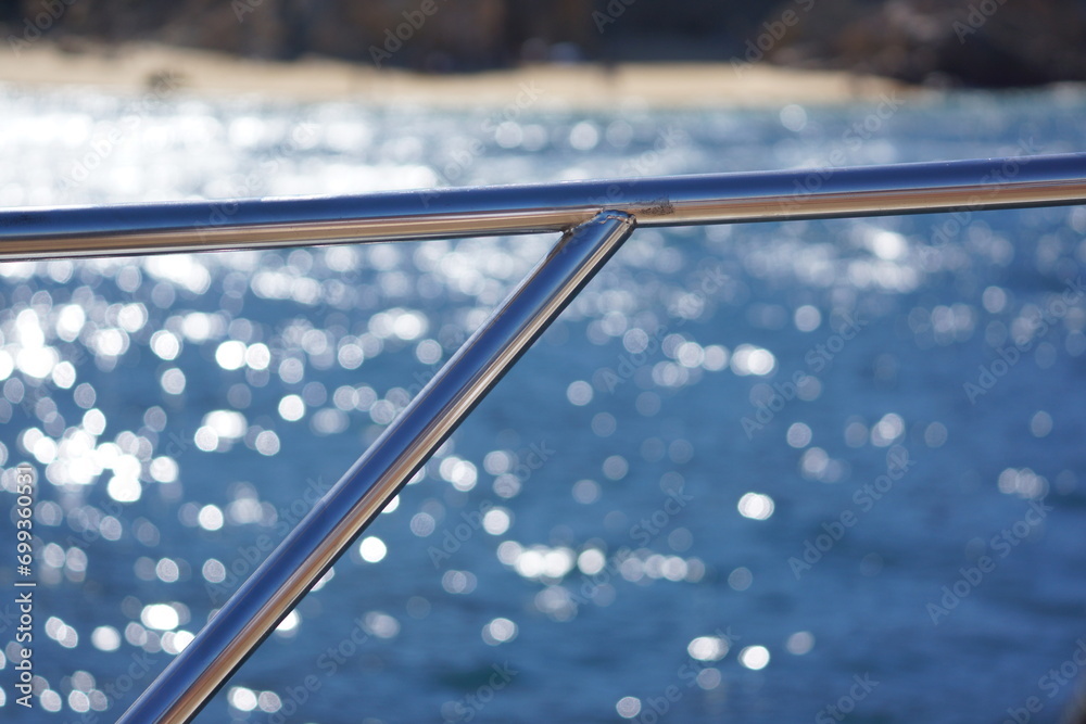 Boat Railing Background Macro of shiny metal rail on boat, ocean and rocky beach in background ...