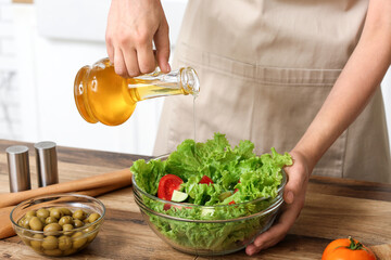 Woman adding olive oil into bowl with tasty salad at table in kitchen