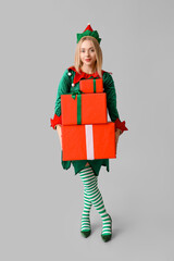 Poster - Young woman in elf costume holding Christmas gift boxes on white background