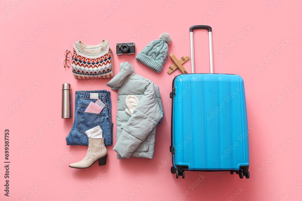 Suitcase with warm clothes, thermos and camera on pink background. Winter vacation concept