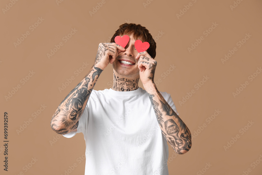 Funny young man with paper hearts on beige background