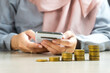 muslim businesswoman using a smartphone or tablet with a heap of coins money in the front, symbol for sharia financial banking investment dividend from business growth concept.