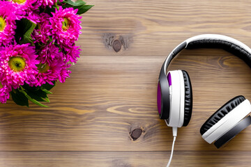 creative composition. on a dark wooden table there is a bouquet of bright pink flowers and large gray headphones