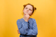 Portrait of thoughtful preteen girl kid contemplating about idea, touching her chin, posing isolated over plain yellow color background wall in studio. Hmm, let's think. Pensive and brainstorm concept