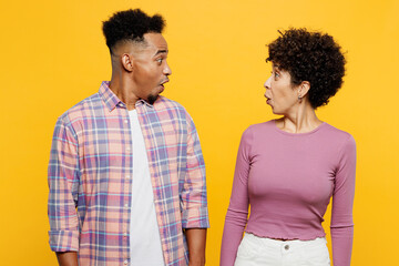 Wall Mural - Young stupefied surprised astonished couple two friend family man woman of African American ethnicity wear purple casual clothes together look to each other isolated on plain yellow orange background