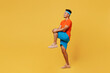 Full body young fitness trainer sporty man sportsman wearing orange t-shirt raise up leg do stretch exercise spend time in home gym isolated on plain yellow background. Workout sport fit abs concept.