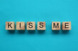 © New Africa - Wooden cubes with phrase Kiss Me on light blue background, flat lay