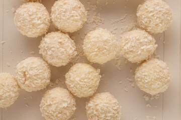 Several candies with nuts and coconut flakes in a paper box, macro, top view.