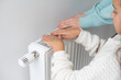 Girl warm one's hands near radiator at home.