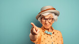 Fototapeta  - Funny old senior woman or grandma wearing a pink shirt, smiling and pointing her finger at the camera. Aged female with glasses, funny elderly retired pensioner with gray hair. Light green wall behind