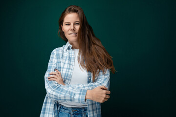 A pretty young woman with brown eyes is wearing a checkered blue shirt and looks confidently at the camera