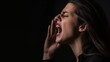 A photo of a woman shouting or screaming for help in profile and holding one hand near the mouth on dark background