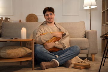 Wall Mural - Young man with warm plaid and pillow sitting at home in evening