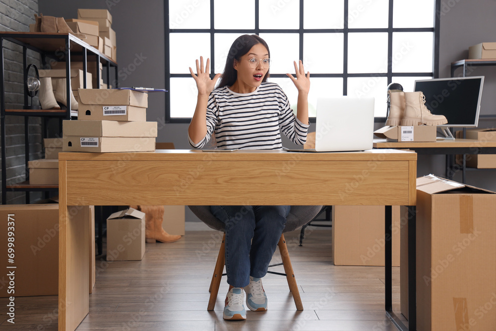 Surprised Asian seller working at table in warehouse store